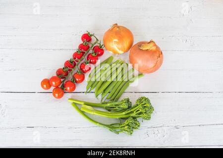 Tenderstem Broccoli, Zwiebeln, Tomaten und grüne Bohnen, auf einem weiß bemalten Brett aus dem Wintergarten ausgelegt. Stockfoto