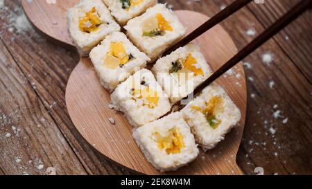 Sushi-Lieferung. Süße Brötchen aus Reis, Ananas, Kiwi und Mango. Rollt auf einem hölzernen Hintergrund. Holzstöcke für Sushi. Stockfoto