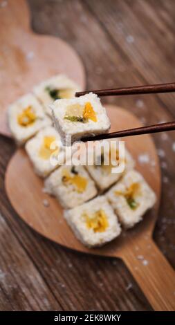 Sushi-Lieferung. Süße Brötchen aus Reis, Ananas, Kiwi und Mango. Rollt auf einem hölzernen Hintergrund. Holzstöcke für Sushi. Stockfoto