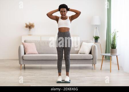 Unzufriedene Afroamerikanische Frau, Die Zu Hause Auf Einer Waage Steht Stockfoto