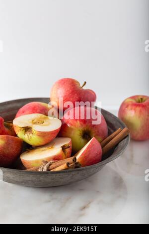 Ganze und in Scheiben geschnittene frische Äpfel mit Zimtstangen auf Marmorboden. Stockfoto