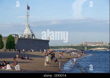 Menschen, die sich am Strand am Fluss Newa gegen die Naryschkin-Bastion der Festung St. Peter und Paul in St. Petersburg, Russland, ausruhen Stockfoto