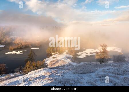 Nebliger gefrorener See an einem knackigen Winternachmittag mit Nebelbogen. Blick auf Tarn Hows im Lake District, Großbritannien. Stockfoto