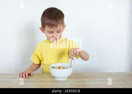 Kleiner Linkshänder Junge in einem gelben T-Shirt essen Obstsalat und lächeln. Kinder gesunde Ernährung Konzept. Ernährungsprodukte. Gesundheitswesen Stockfoto