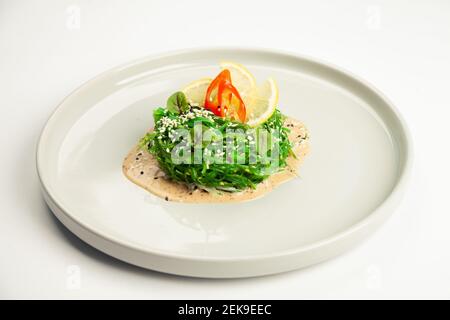 Chuka Salat auf einem Teller. Zutaten marinierte Algen, Erdnusssauce, Zitrone, Chili, Sesammischung. Für die Speisekarte des Restaurants. Stockfoto