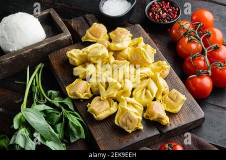 Hausgemachte Tortellini mit Käse und Basilikum Set, auf Holz Schneidebrett, auf alten dunklen Holztisch Hintergrund Stockfoto