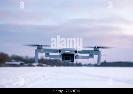 Kharkiv, Ukraine - 21. Februar 2021: DJI Mavic Mini 2 Drohne fliegen im Winter verschneite Landschaft in Sonnenuntergang lila Wolken. Neue Quadcopter Gerät schwebend Stockfoto