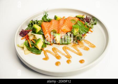 Lachs- und Avocado-Salat in Tamarindensauce auf einem Teller. Zutaten Eisbergsalat, Lachs, Avocado, Spinat, Karotte, Tamarindensoße. Für die Speisekarte des Restaurants. Stockfoto