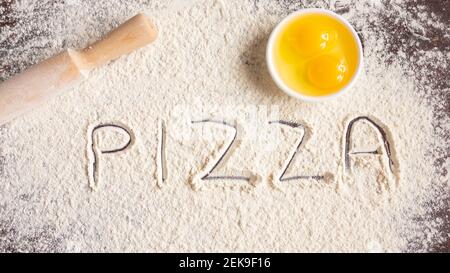 Die Inschrift Pizza auf bestreut Mehl, auf einem hölzernen Hintergrund gezeichnet, Nudelholz und Eier. Backrezepte. Stockfoto
