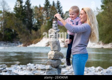 Mutter trägt Sohn beim Balancieren von Steinhaufen am Flussufer Stockfoto