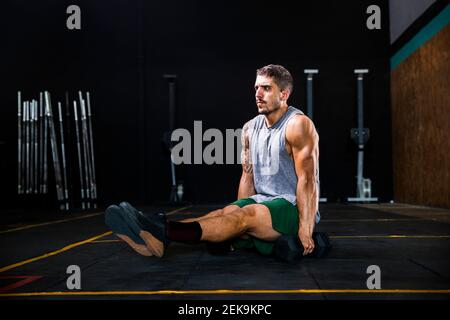 Muskulöser junger Mann mit Hanteln, die im Fitnessstudio über dem Boden balancieren Stockfoto