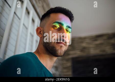 Regenbogenlicht trifft Gesicht des jungen Mannes, der unten schaut Kamera Stockfoto