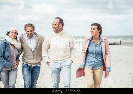 Gruppe von erwachsenen Freunden, die Seite an Seite entlang des Sandstrandes gehen Strand Stockfoto