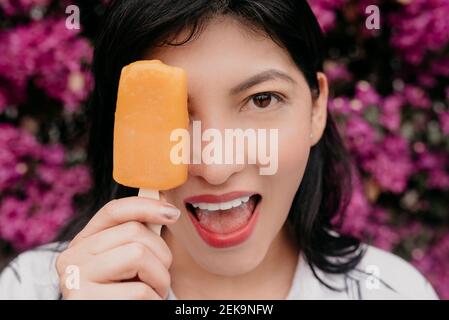 Glückliche Frau mit offenem Mund, das Auge mit orangefarbenem Eis bedeckt Creme Stockfoto
