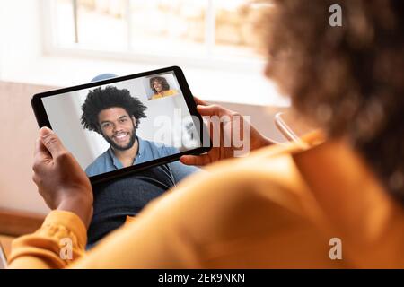 Frau im Gespräch mit lächelndem Mann auf Videoanruf durch digital Tablet, während Sie zu Hause sitzen Stockfoto