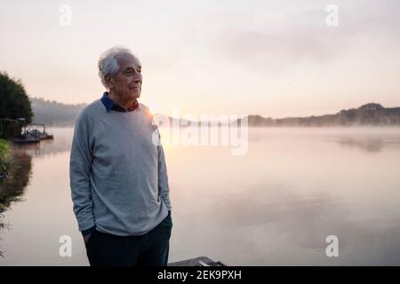 Älterer Mann mit Blick auf die Aussicht, während er gegen den See steht sonnenaufgang Stockfoto