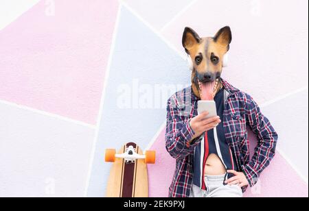 Frau trägt Hundemaske mit Handy, während Sie stehen Skateboard gegen Wand Stockfoto