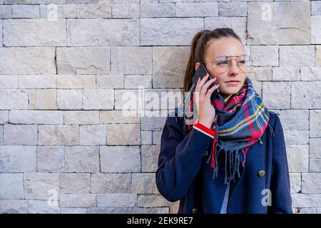 Teenager-Mädchen tragen warme Kleidung reden über Smartphone gegen Backsteinmauer zu Hause Stockfoto