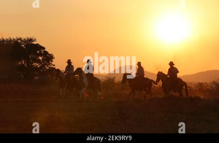 Die Silhouette von Reiter als Cowboy Outfit Kostüm mit einem Pferde und ein Gewehr in der Hand gegen Rauch gehalten Und Sonnenuntergang Hintergrund Stockfoto