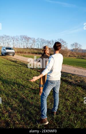 Heterosexuelles Paar mit ausgestreckten Armen auf grünem Land stehend während Sonnenuntergang Stockfoto