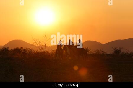 Die Silhouette von Reiter als Cowboy Outfit Kostüm mit einem Pferde und ein Gewehr in der Hand gegen Rauch gehalten Und Sonnenuntergang Hintergrund Stockfoto