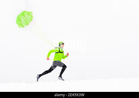 Männlicher Athlet mit Fallschirm, der im Winter auf Schnee läuft Stockfoto