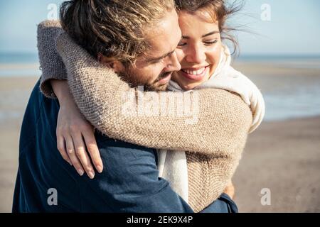 Glückliches junges Paar umarmt am Strand an sonnigen Tag Stockfoto
