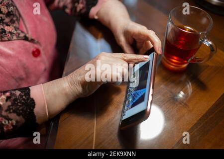 Ältere Frau berührt Bildschirm des Mobiltelefons auf dem Tisch bei Zu Hause Stockfoto