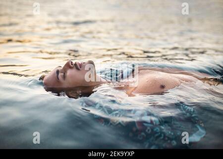 Junger Mann mit geschlossenen Augen schwimmend im Wasser Stockfoto