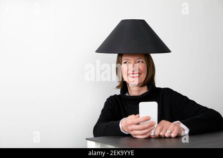 Glückliche Frau trägt schwarzen Lampenschirm mit Smartphone suchen Weg Stockfoto