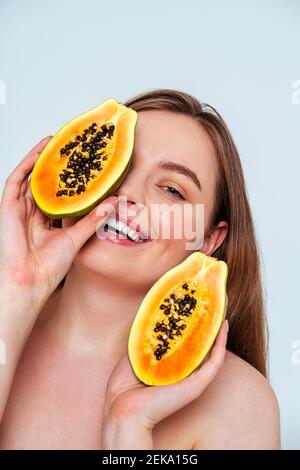 Nahaufnahme einer lächelnden schönen Frau, die Papaya-Scheiben gegen Weiß hält Hintergrund Stockfoto