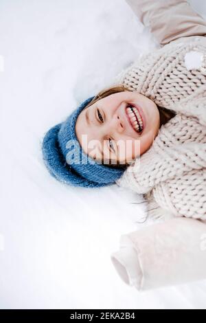 Fröhliches Mädchen mit Schal liegen auf Schnee im Winter Stockfoto