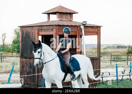 Mittlere Erwachsene Frau Reiten auf weißem Pferd auf dem Bauernhof Stockfoto