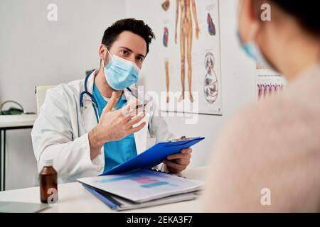 Männlicher Arzt mit Schutzmaske im Gespräch mit dem Patienten in der Klinik Stockfoto