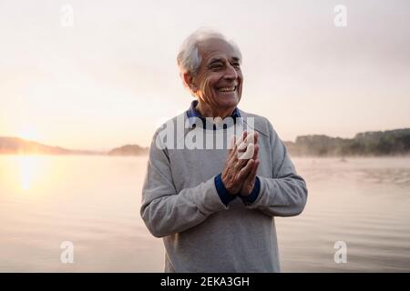 Lächelnder Mann, der mit den Händen gegen den See geklemmt steht Stockfoto