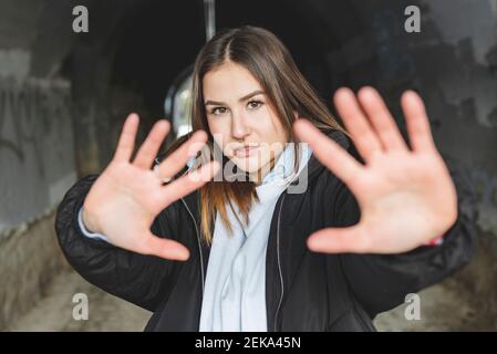 Junge Frau mit Jacke, die die Hand streckt, während sie gegen die Unterführung steht Stockfoto