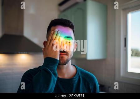 Regenbogen Licht trifft Gesicht von jungen Mann, die ein Auge mit Hand Stockfoto