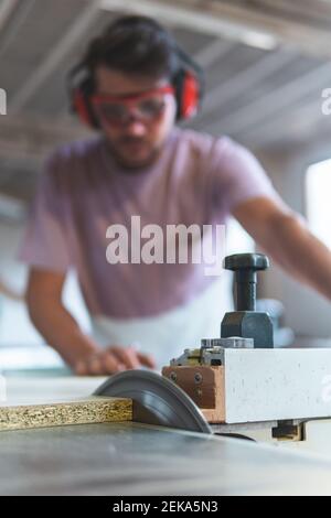 Männlicher Zimmermann schneidet Holz mit Tischsäge während der Arbeit in Werkstatt Stockfoto