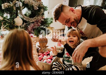 Tochter verzieren Weihnachtsbaum, während in hockender Position mit Vater zu Hause Stockfoto