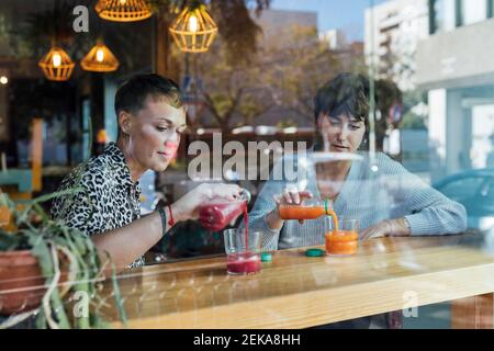 Junge Frauen trinken in Glas, während sie beim Restaurant sitzen Angezeigt Stockfoto