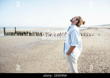 Junger Mann mit geschlossenen Augen steht am Wochenende am Strand Stockfoto