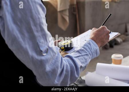 Nahaufnahme eines männlichen Architekten, der auf einem Dokument im Gebäude schreibt Stockfoto