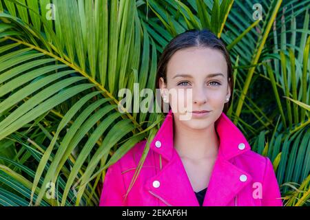 Nahaufnahme eines Teenagers mit rosa Mantel gegen Pflanzen in Hof Stockfoto