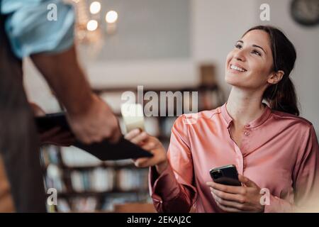 Lächelnde Kundin, die mit Kreditkarte an den männlichen Kellner zahlt Im Café Stockfoto