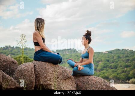 Flexible weibliche Ausbilderin und junge Frau, die Yoga auf Rock praktiziert Gegen den Himmel Stockfoto