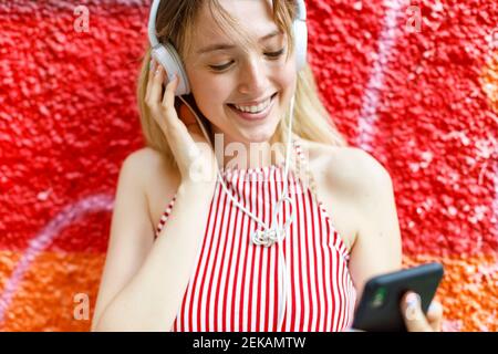 Junge Frau, die Musik hört, während der Tag vor der bunten Wand träumt Stockfoto