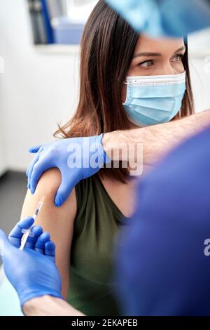 Patientin, die in der Klinik eine COVID-19-Impfung am Arm mit einer schützenden Gesichtsmaske durchgeführt hat Stockfoto