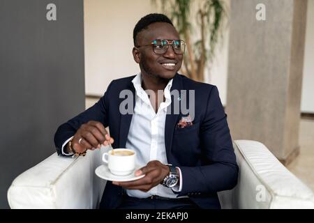 Lächelnder männlicher Profi, der wegschaut, während er die Kaffeetasse in der Hand hält Hotellobby Stockfoto