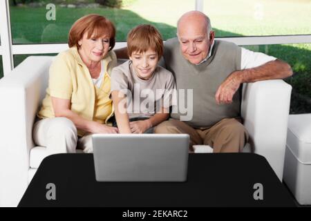 Junge sitzt mit seinen Großeltern mit einem Laptop Stockfoto