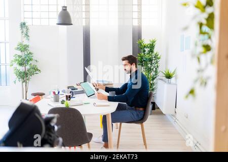 Männlicher Unternehmer, der Dokumente überprüft, während er im Büro auf einem Stuhl sitzt Stockfoto